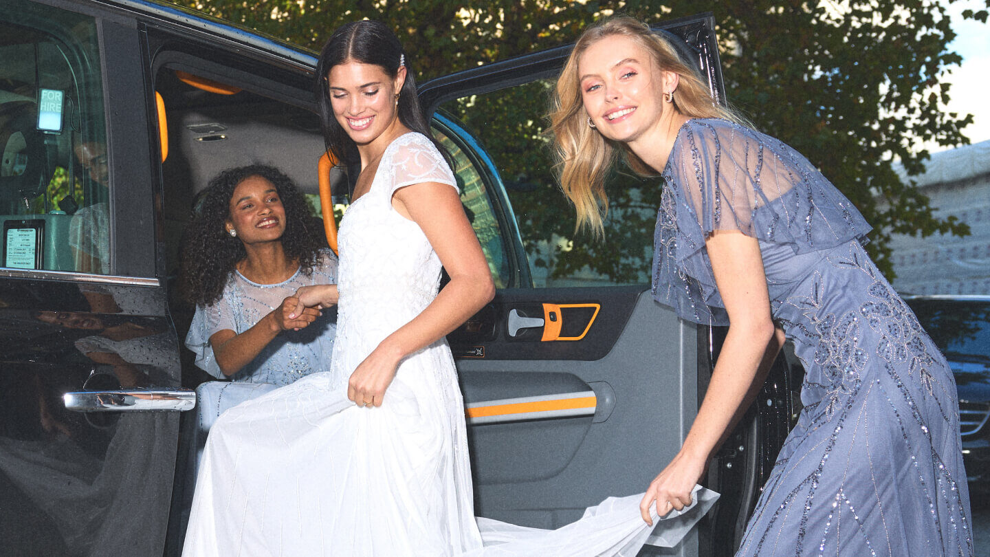 Bride gets into a taxi with the help of her two friends in blue embroidered bridesmaid dresses